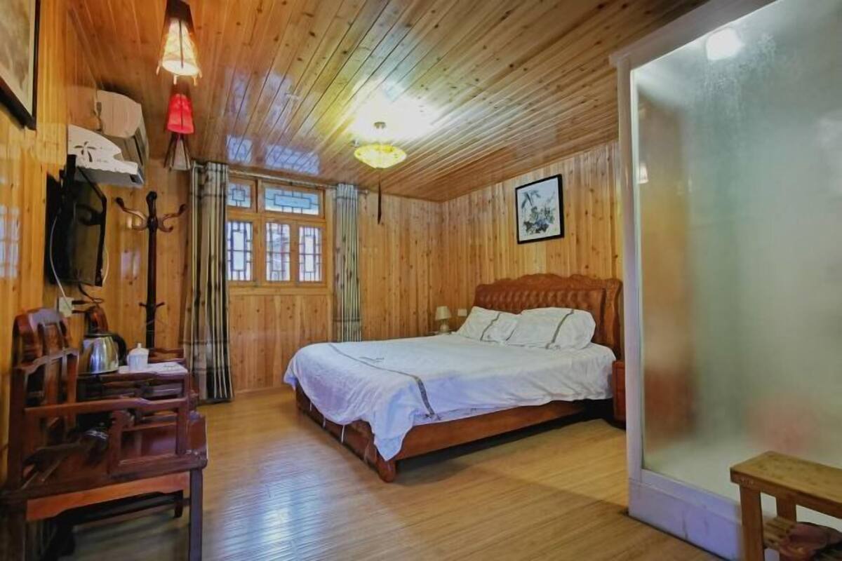 A wooden-paneled room with a bed, a chair, a table, and a window.