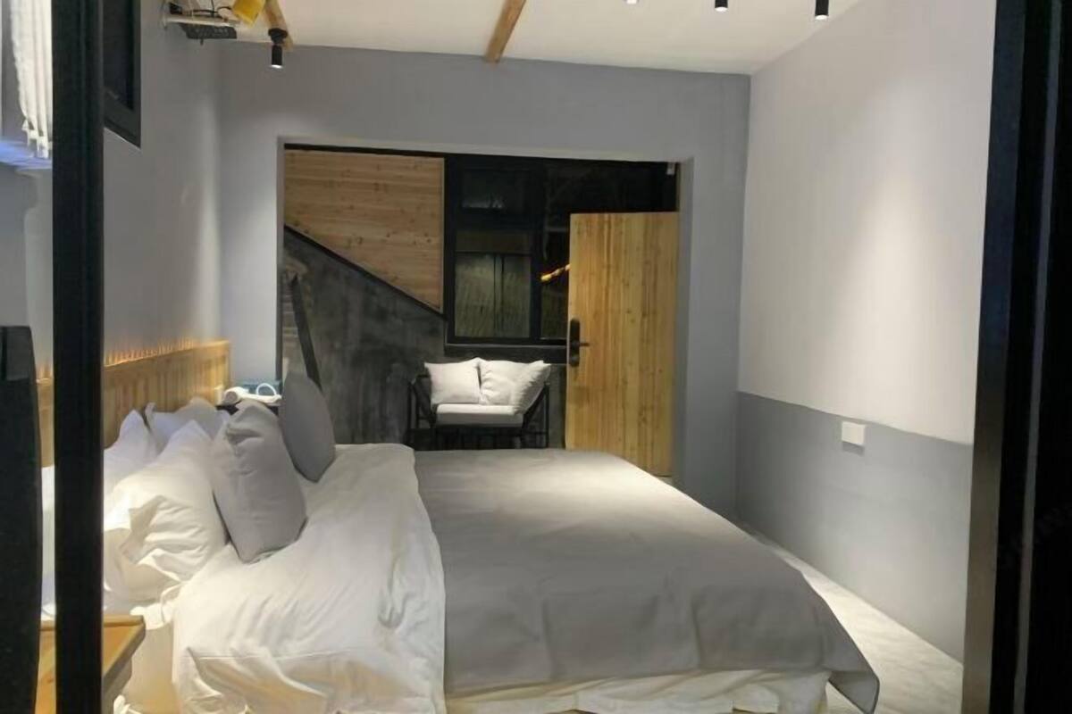 A bedroom with a bed, a chair, and a staircase leading to another room.