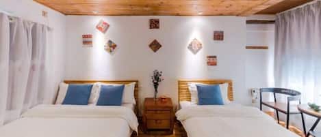 Une chambre avec deux lits, un plancher en bois, un ventilateur de plafond et des œuvres d’art décoratives au mur.