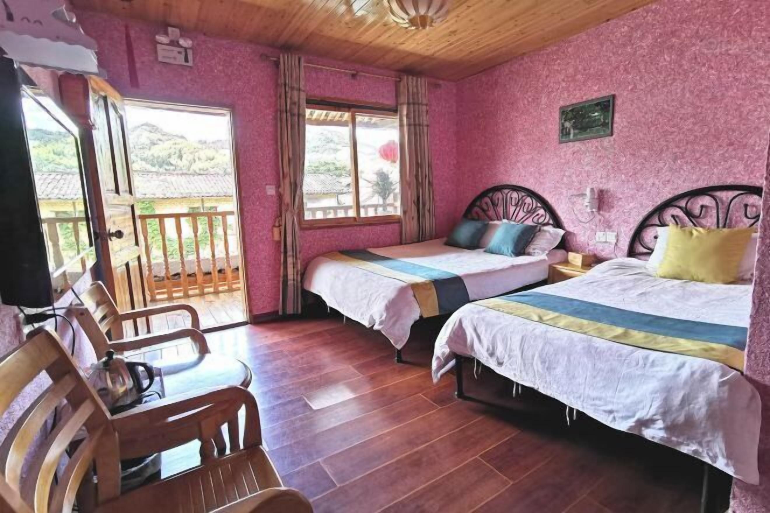 A room with two beds, wooden flooring, a balcony, and a view of the outdoors.