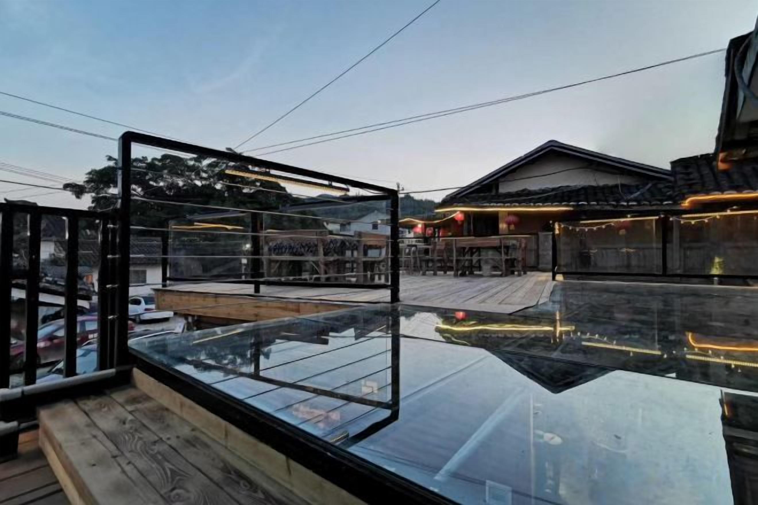 A modern building with a reflective glass facade, a wooden deck, and a traditional structure in the background.