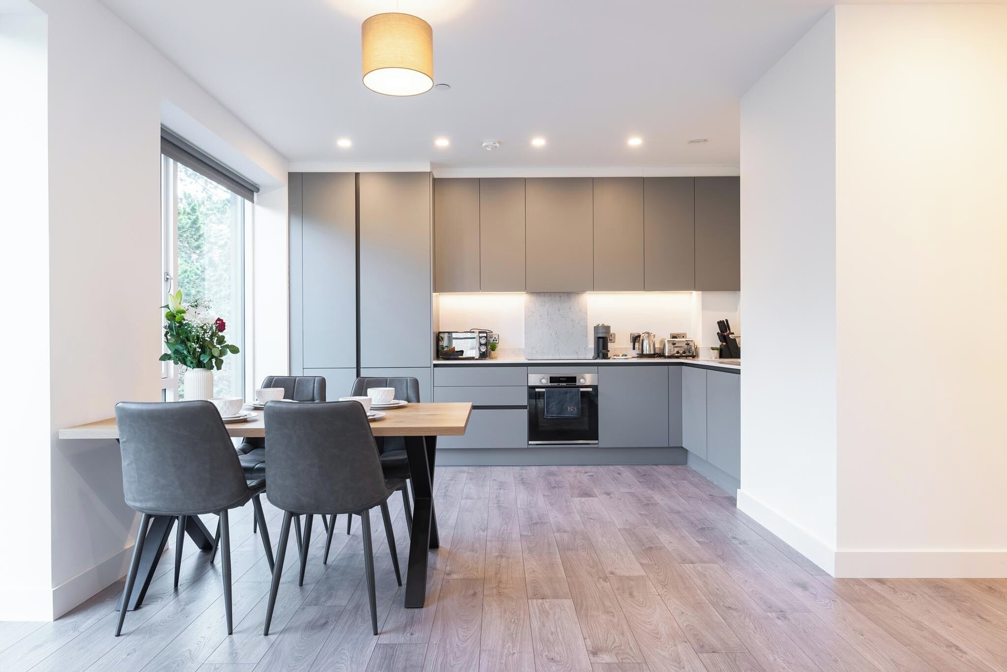 A modern kitchen with grey cabinets, a wooden dining table, and chairs.