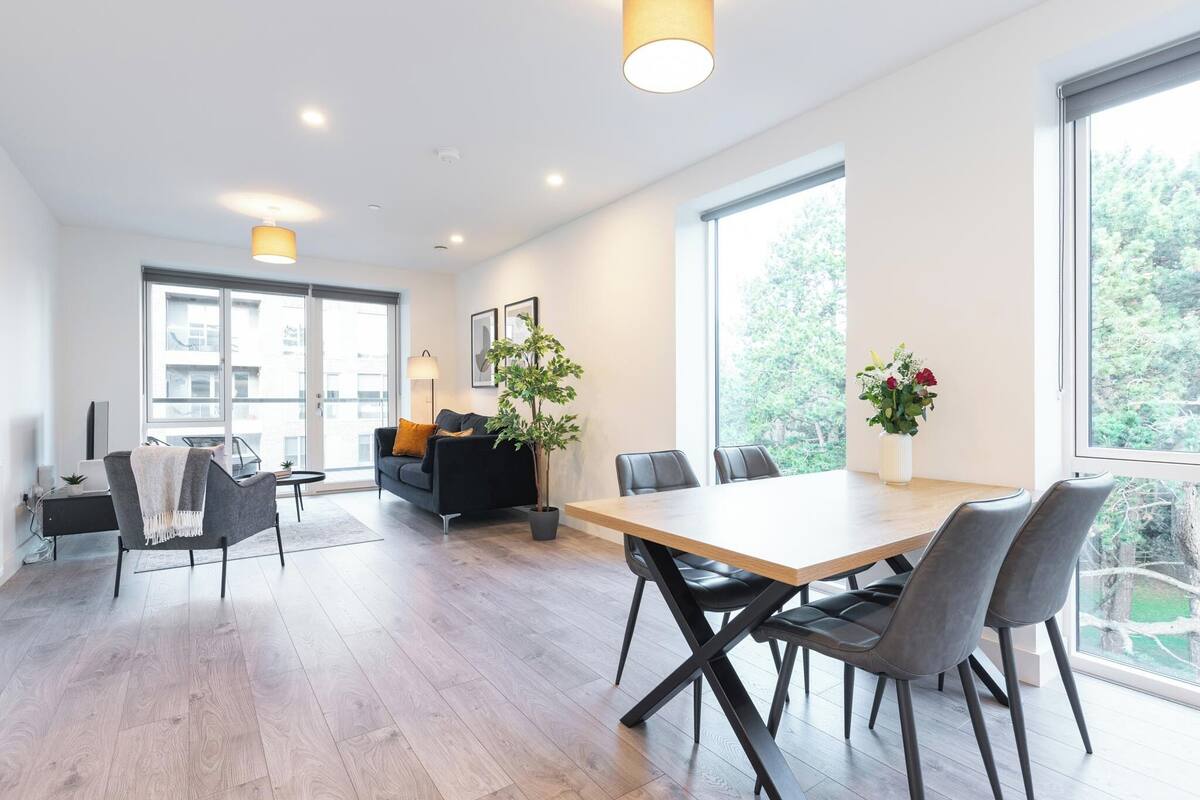 A modern living room with a dining area, large windows, and a potted plant.