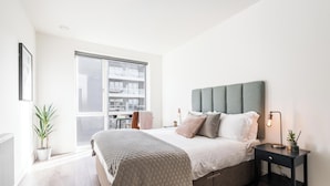 A modern bedroom with a large bed, a nightstand, a potted plant, and a view of a cityscape through a large window. - Urban Rest - Dublin Port (Dublin)