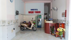 Entrada de un motel con una scooter estacionada adentro, un refrigerador y un mostrador de recepción.