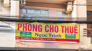 A building with a sign for 'Phong Cho Thu' and 'Ngoc Trinh' indicating a 24/7 service. There is a visible entrance with a gate and a sign for a motel with operating hours. - Ngoc Trinh Hotel Binh Tan by Zuzu (Ho Chi Minh Municipality)