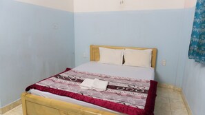 Una cama individual con cabecera de madera, ropa de cama blanca y una colcha roja y blanca estampada.