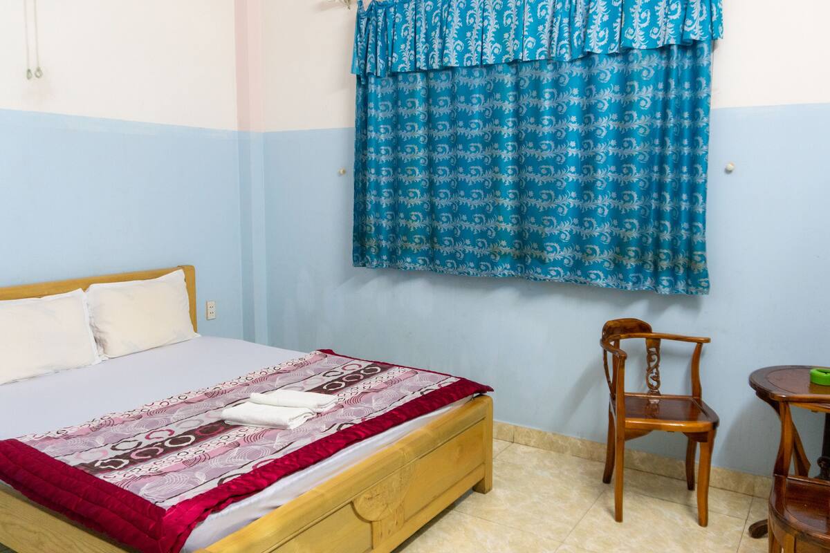 Un dormitorio con una cama de madera, una silla, una mesita y una cortina estampada.