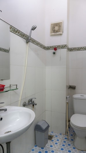 Un baño con lavamanos blanco, inodoro y ducha con manguera.
