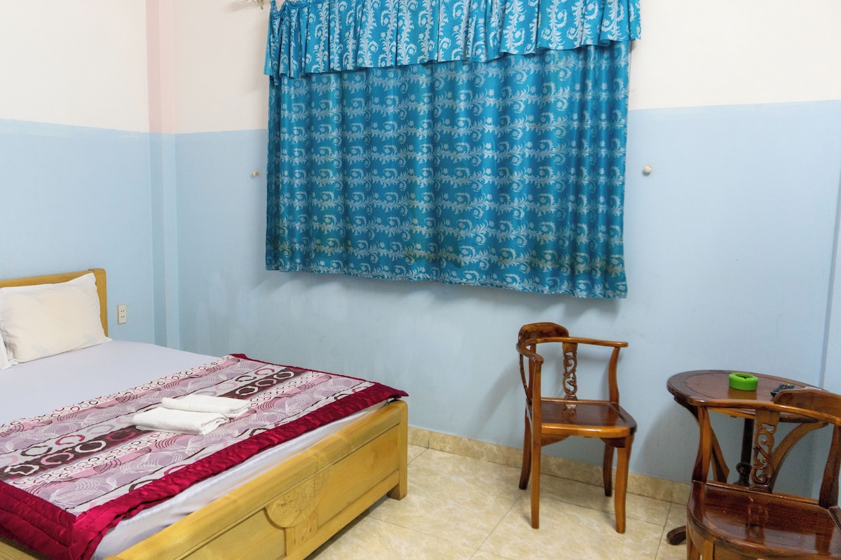 Un dormitorio con una cama, una silla, una mesita y un ventanal con cortinas.