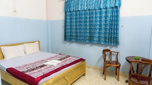 Un dormitorio con una cama de madera, una silla, una mesita y una cortina estampada.