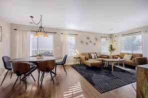 A modern living room with a dining area, wooden flooring, and large windows.