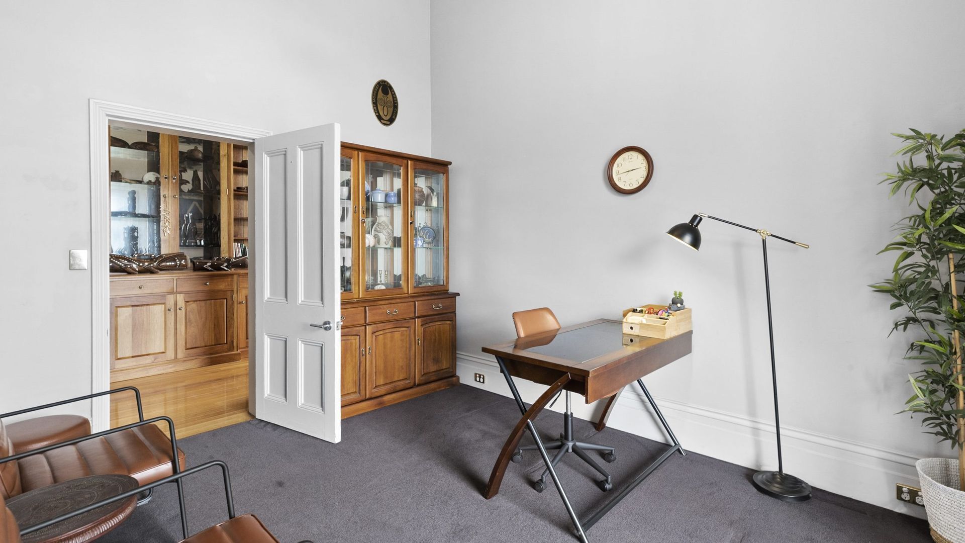 A room with a desk, chair, lamp, clock, cabinet, and a plant.
