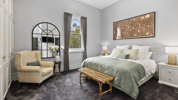 A bedroom with a bed, a chair, a bench, a nightstand, a lamp, a mirror, and a wall art piece.
