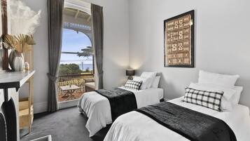 A hotel room with two beds, a view of the sea, a table with a vase, and a decorative wall piece.