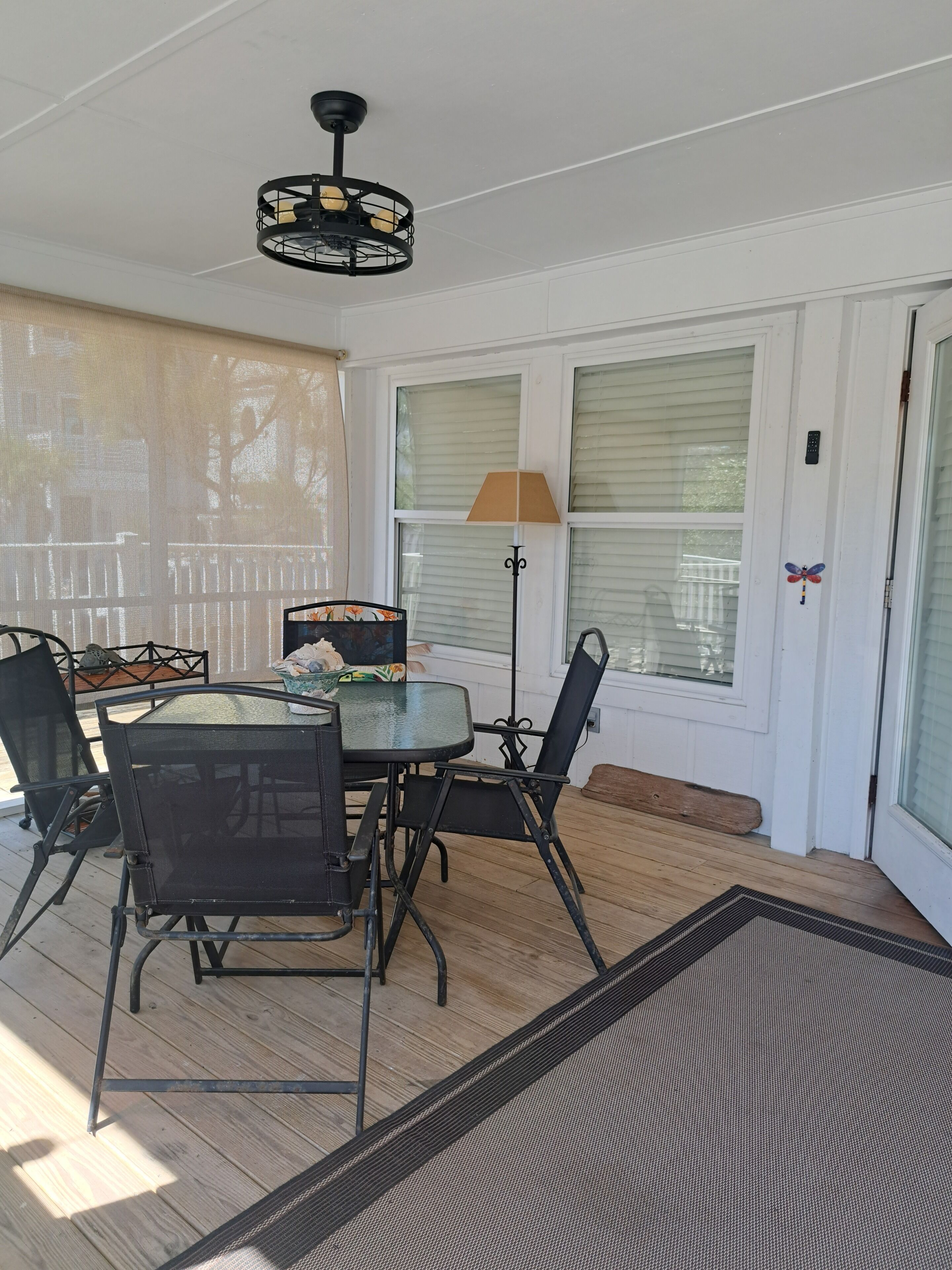 Une terrasse couverte avec une table et des chaises, un ventilateur de plafond et une vue à travers les fenêtres.
