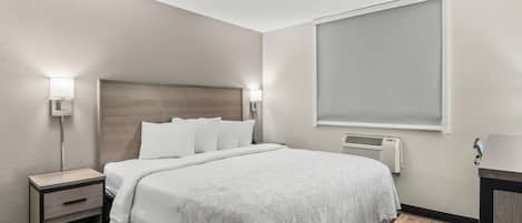 A hotel room with a bed, bedside tables, a window, and a wall-mounted air conditioner.
