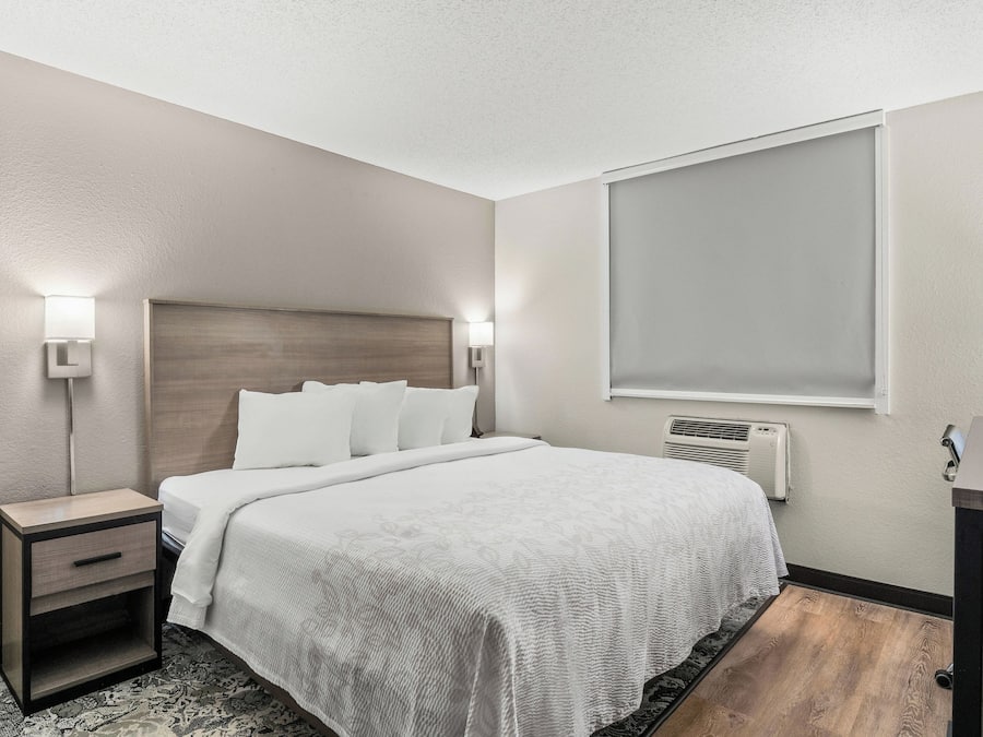 A hotel room with a bed, bedside tables, a window, and a wall-mounted air conditioner.