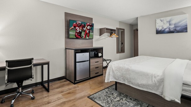 Habitación de hotel con cama, escritorio con silla, minibar y obras de arte en las paredes.