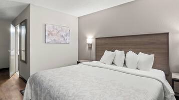 A hotel room with a large bed, a headboard, a bedside table, a nightstand, a wall-mounted lamp, and a door leading to another room.