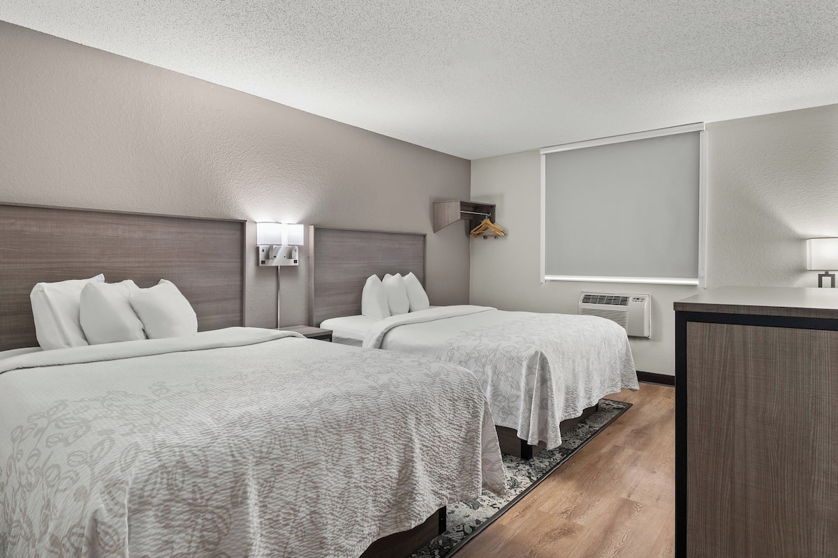 A hotel room with two beds, a desk, a chair, a wardrobe, and a window with blinds.