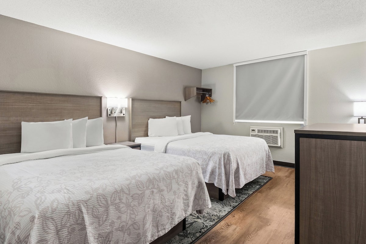 A hotel room with two beds, a desk, a wardrobe, and a large window.