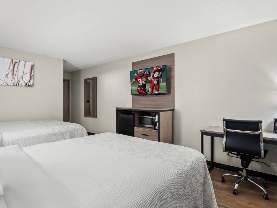 A hotel room with two beds, a desk with a computer, a TV, and a microwave.