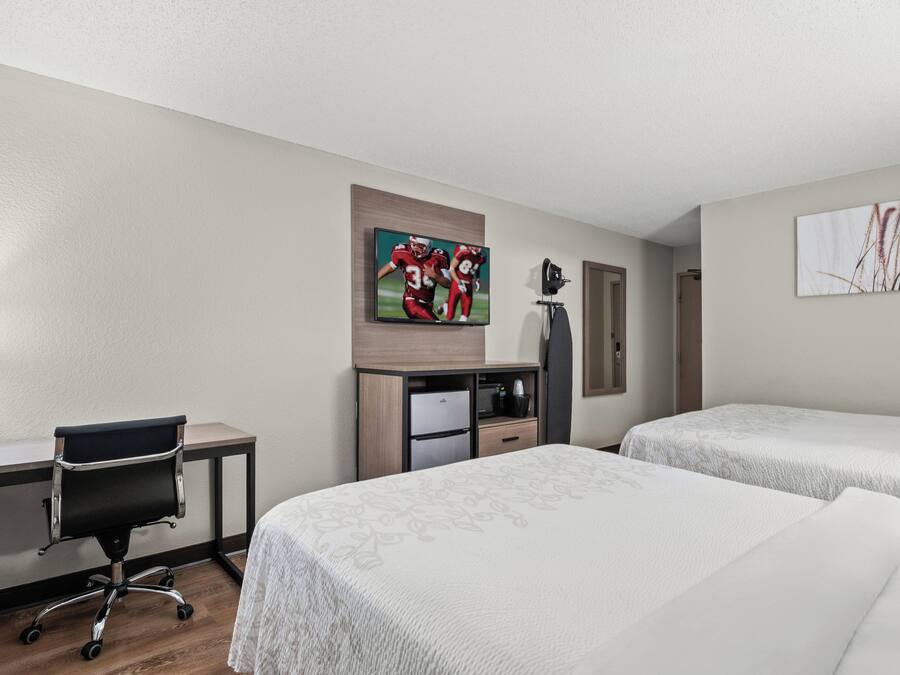 A hotel room with two beds, a desk, a chair, a TV, and artwork on the walls.