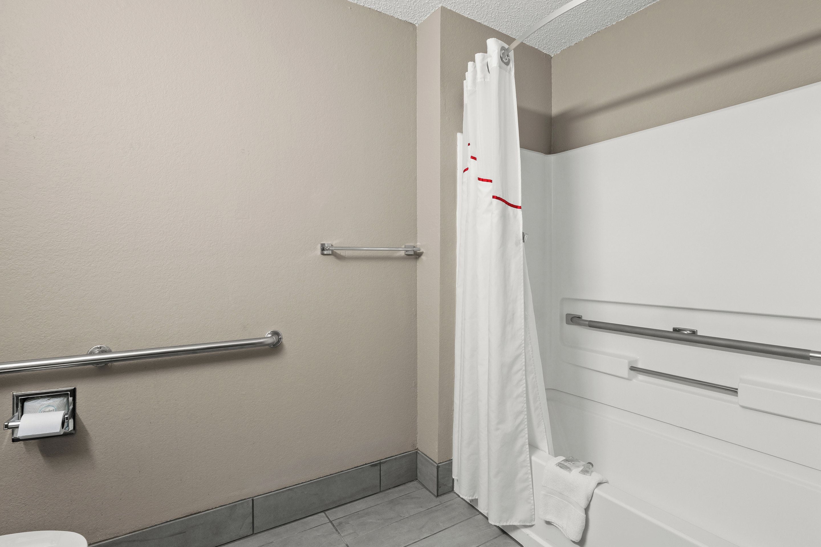 Un baño con inodoro, ducha con cortina blanca y barra de apoyo en la pared.