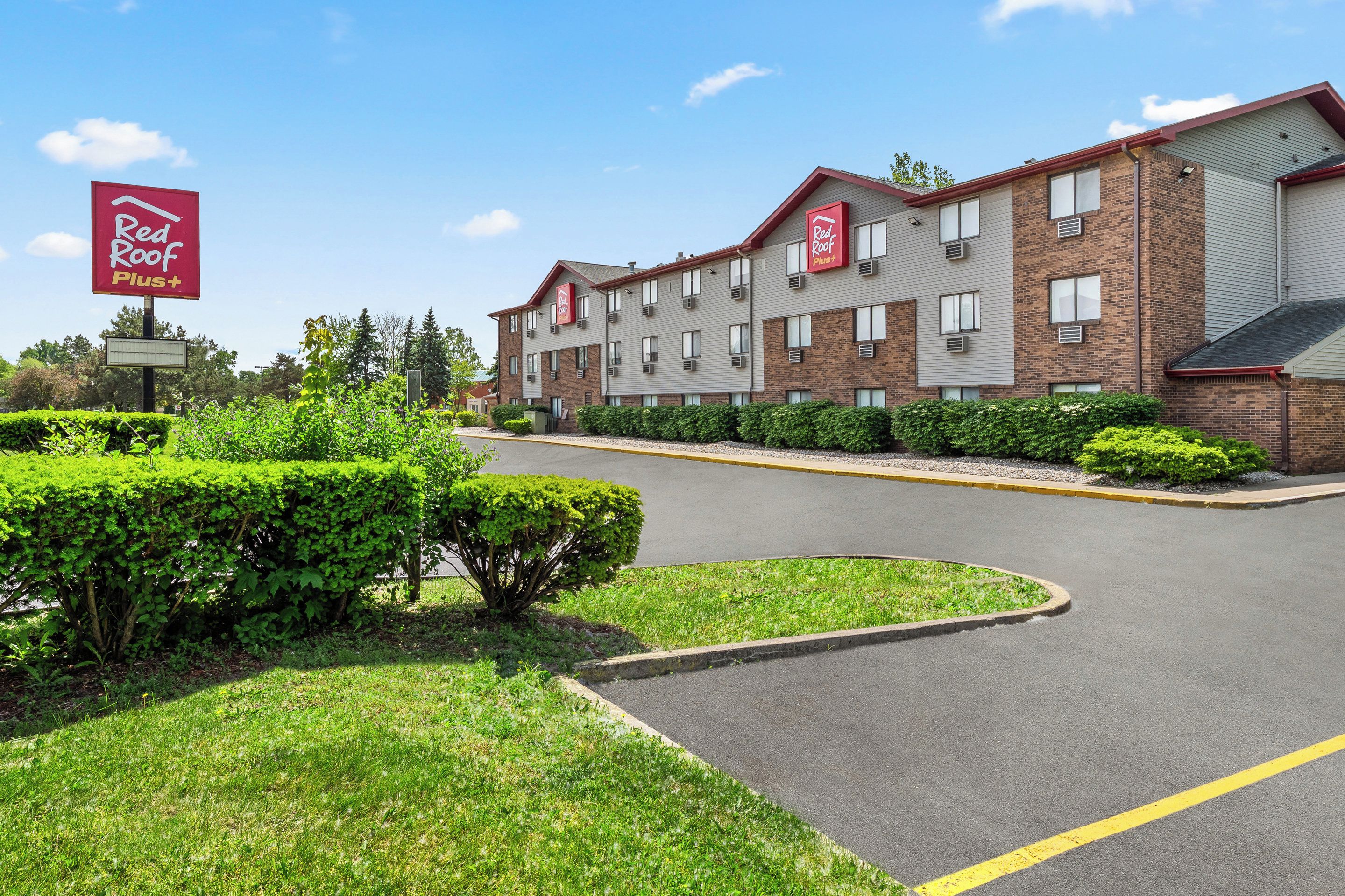 A Red Roof Plus hotel with a brick facade, multiple windows, and a parking lot with a yellow line marking.