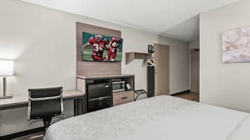 A hotel room with a bed, a desk with a chair, a TV mounted on the wall, and a door leading to another room.