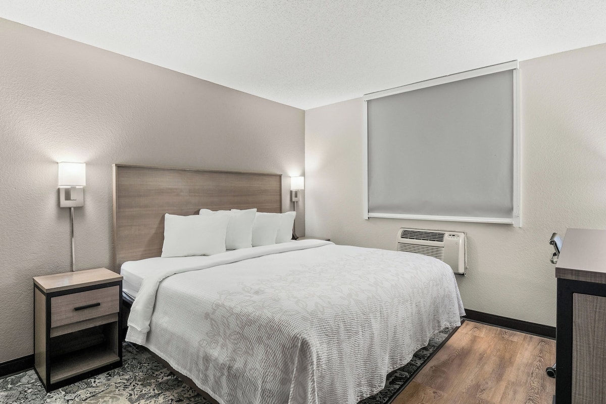 A hotel room with a bed, bedside tables, a window, and a wall-mounted air conditioner.