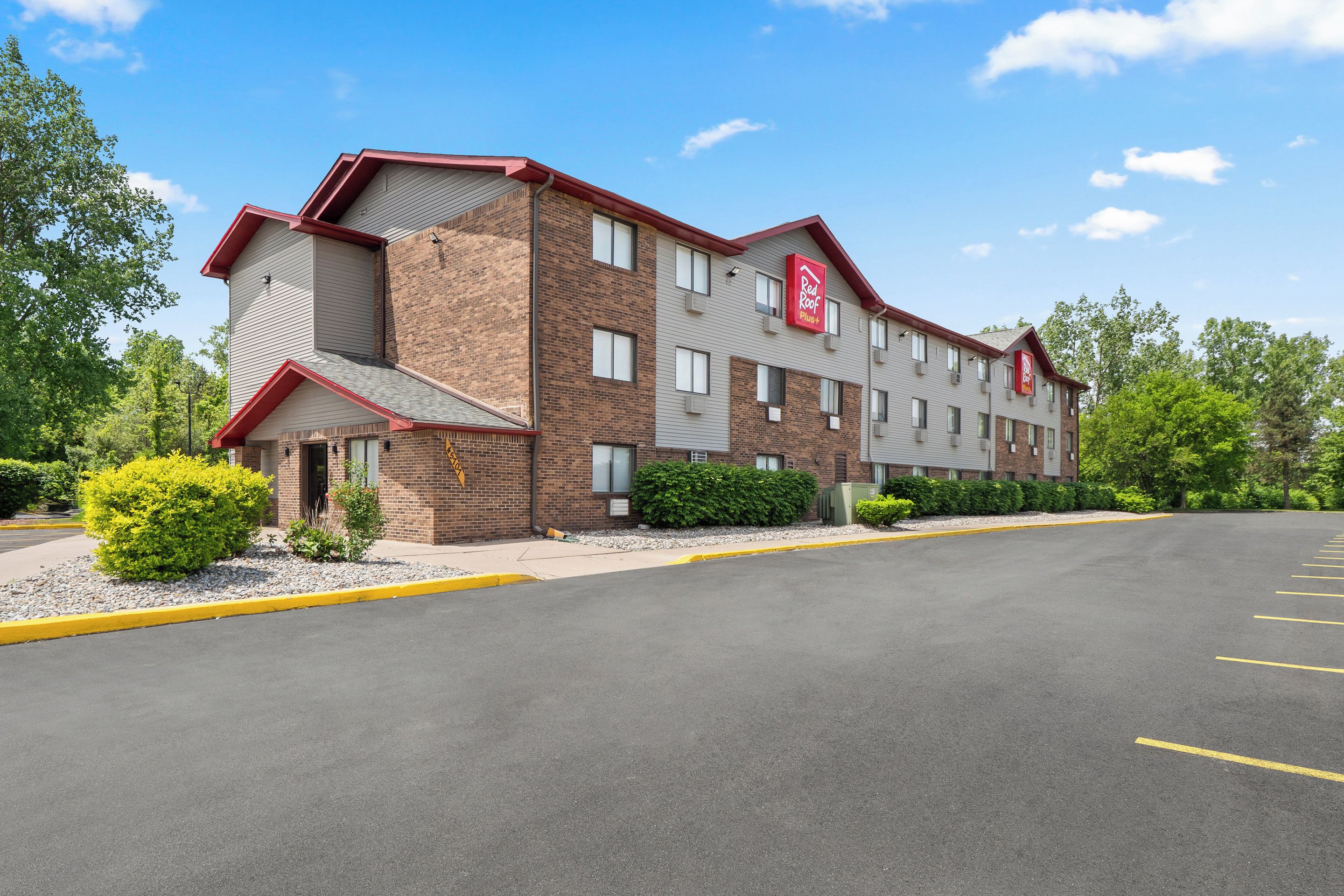 A multi-story hotel with a brick facade, a red and white logo, and a parking lot in front.