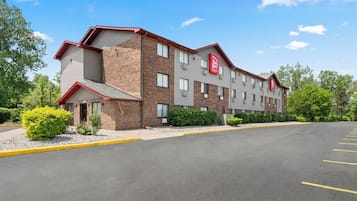 A multi-story hotel with a brick facade, a red and white logo, and a parking lot in front.