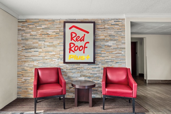 Una habitación con pared de piedra, dos sillas rojas y una pequeña mesa.