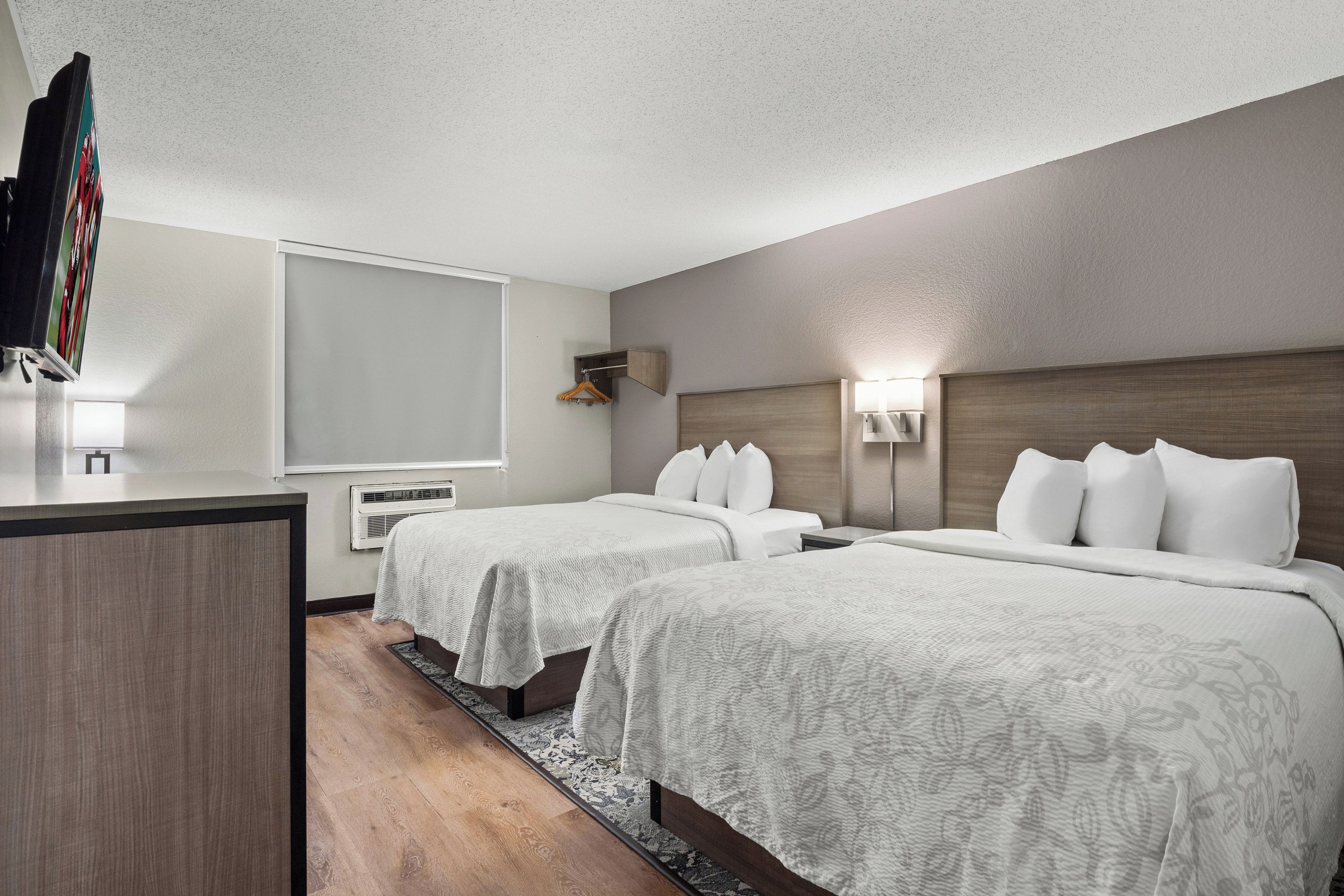 Quarto de hotel com duas camas, uma escrivaninha, televisão e aquecedor fixado na parede.
