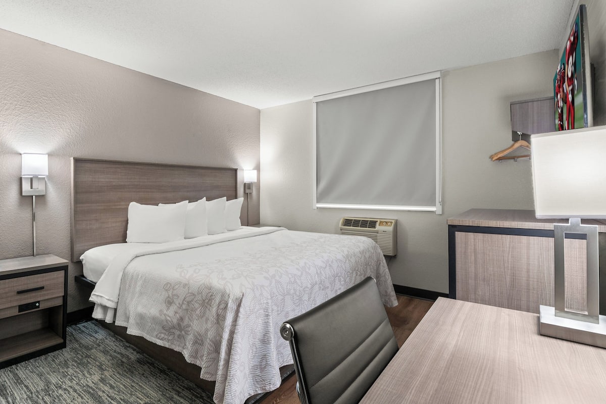A hotel room with a bed, bedside tables, a desk, and a chair.