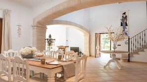 Un coin repas avec une table et des chaises en bois, un lustre et une vue sur l’extérieur grâce à une porte ouverte.