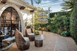 An outdoor seating area with wicker chairs and a decorative umbrella, surrounded by lush greenery and a stone pathway. - Montecito Studio w/ Patio & Outdoor Charm (Montecito)