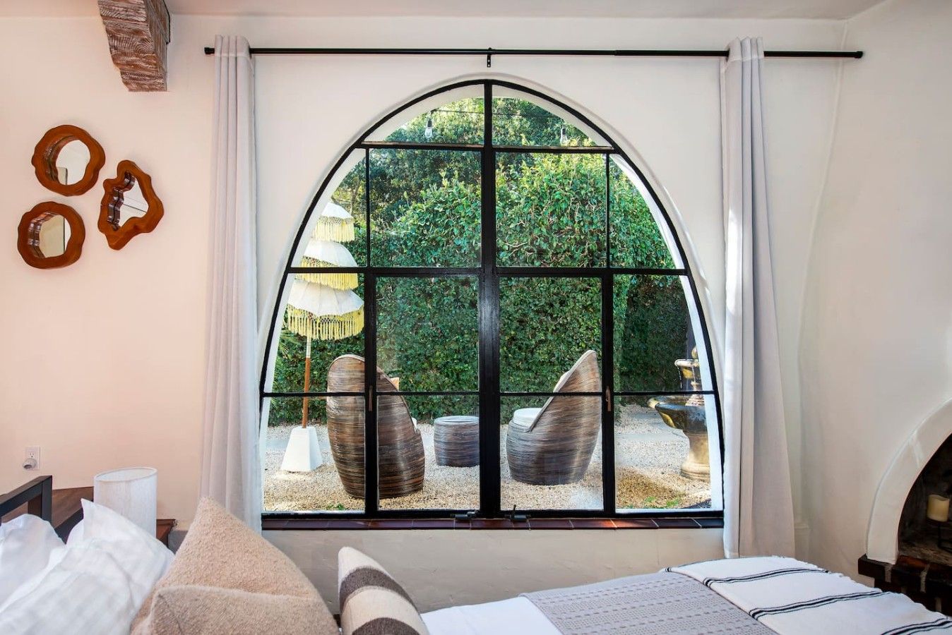 A bedroom with a large arched window, a bed, a bedside table, and a lamp.