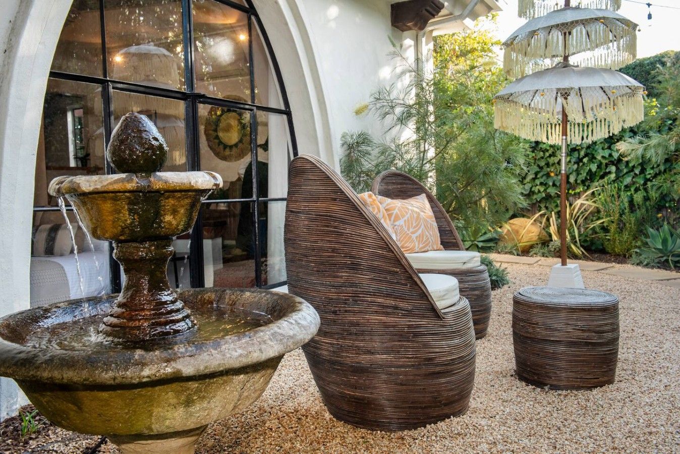 A fountain, wicker furniture, and a decorative umbrella in a garden setting.