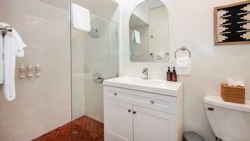 A bathroom with a glass shower enclosure, a white vanity with a mirror, and a toilet.