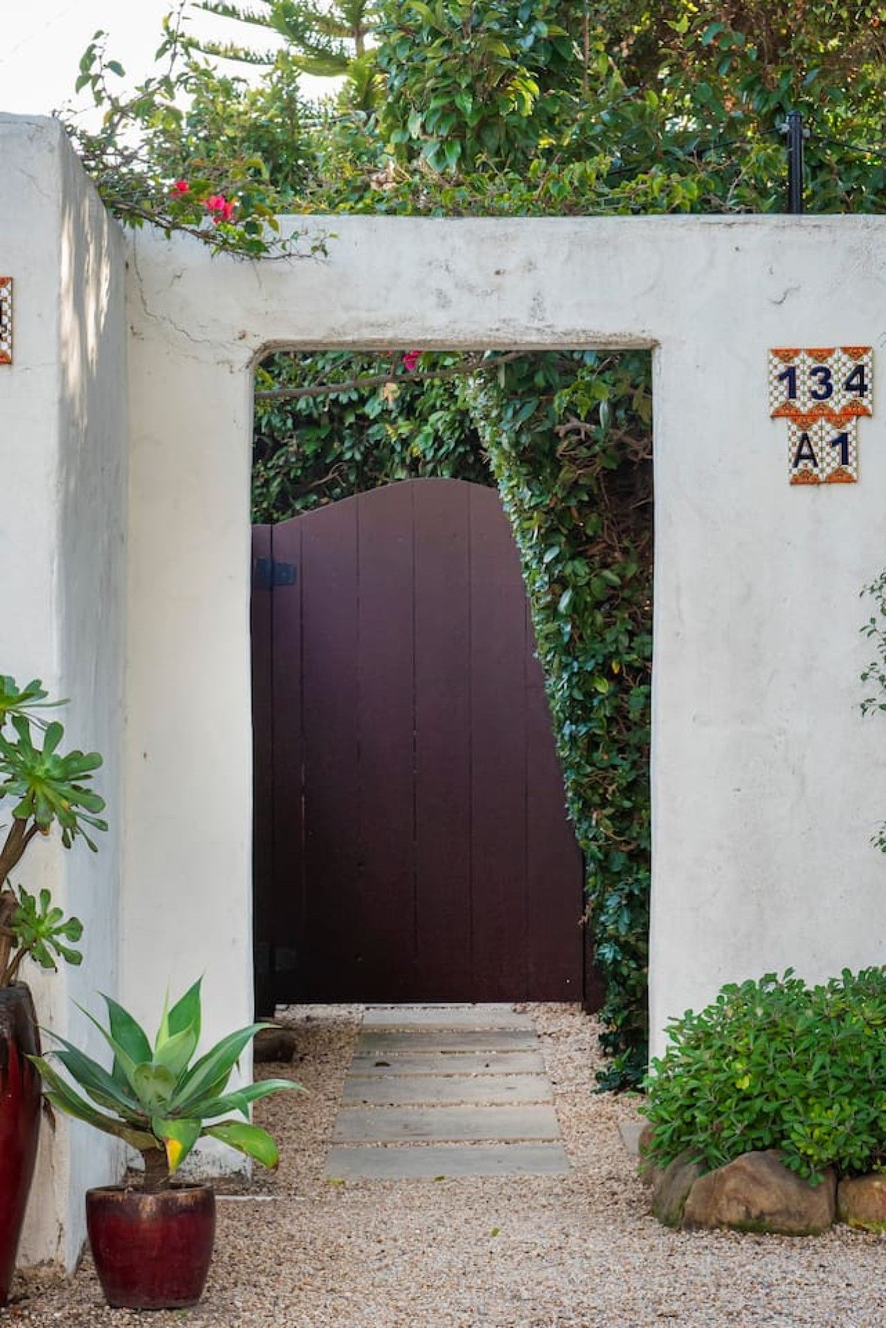 A gated entrance with a number sign, a gravel path, and potted plants.