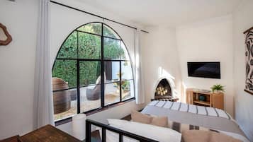 A bedroom with a large arched window, a fireplace, a television, and a wooden bench.