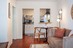 Un espacio habitable compacto con kitchenette, una zona de comedor con mesa y sillas, y una sala de estar con sofá.
