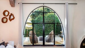 A bedroom with a large arched window, a bed, a bedside table, and a lamp.
