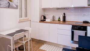 Una cocina moderna con armarios blancos, encimera de madera, un lavamanos y una zona de comedor con mesa y sillas.