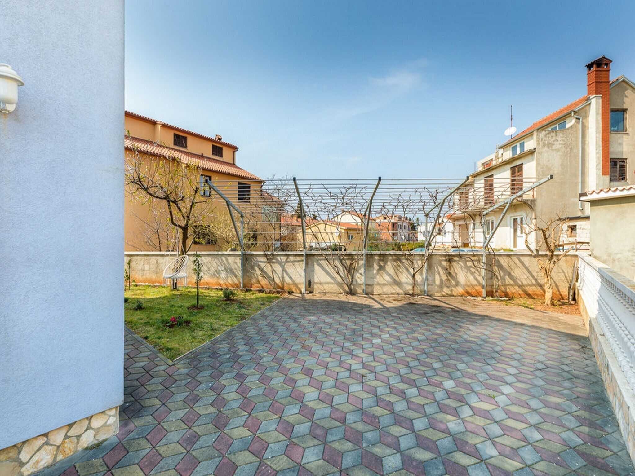 A courtyard with patterned paving, a metal fence, and buildings in the background.