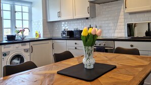 Una cocina moderna con armarios blancos, una mesa de comedor de madera, una encimera negra y un ventanal con vistas al verdor.