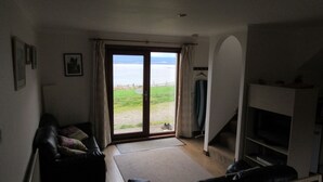 Una sala de estar con sofá, televisión y vista al mar a través de un amplio ventanal corredera.
